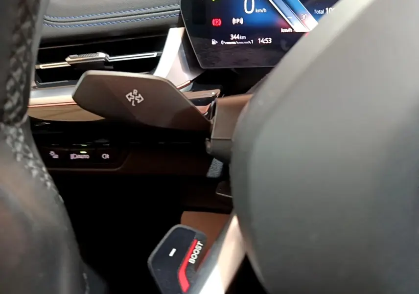 Gros plan sur le volant noir et le levier de commande derrière, avec l'affichage digital du tableau de bord d'une BMW X1 xDrive23i M Sport.