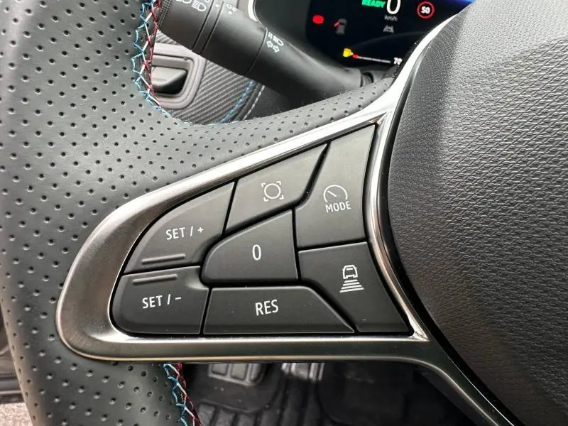 Gros plan sur les commandes au volant perforé du Renault Captur 2026 gris Cassiopée/Noir Étoilé, boutons multifonctions visibles.