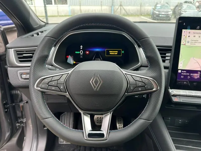 Vue intérieure centrée sur le volant du Renault Captur 2026 hybride, cuir noir avec surpiqûres bleues et tableau de bord digital.