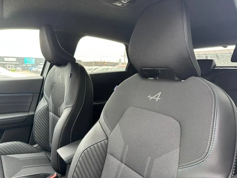 Vue intérieure des sièges avant du Renault Captur 2026 esprit Alpine, tissu gris avec logo Alpine brodé sur appuie-tête.