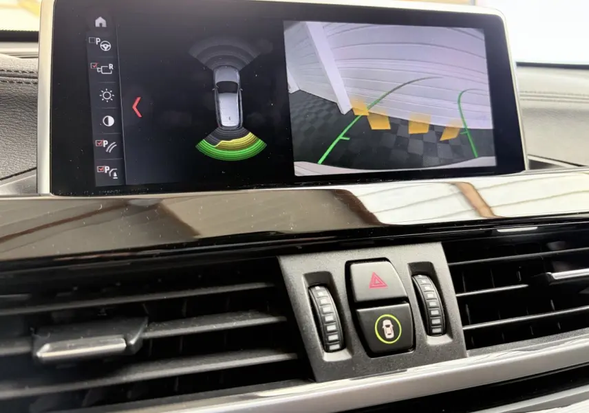 Vue rapprochée de l’écran tactile du tableau de bord du BMW X1 blanc, affichant l’aide au stationnement arrière.