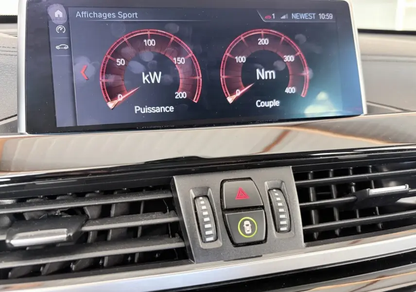 Gros plan sur l'écran tactile et la console centrale noire du tableau de bord du BMW X1 blanc, affichant les données de puissance et couple.