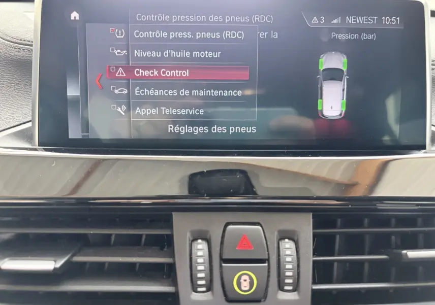 Écran tactile central du tableau de bord du BMW X1 blanc, affichant le menu de contrôle pression des pneus.