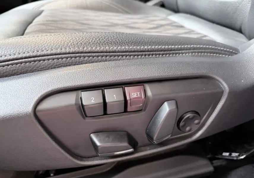 Détail des commandes de réglage électrique des sièges en cuir noir à gauche dans l’habitacle du BMW X1 blanc.