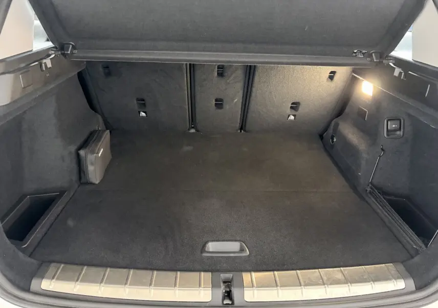 Coffre ouvert du BMW X1 blanc, vue intérieure arrière montrant un espace de chargement propre avec tapis noir et éclairage latéral.