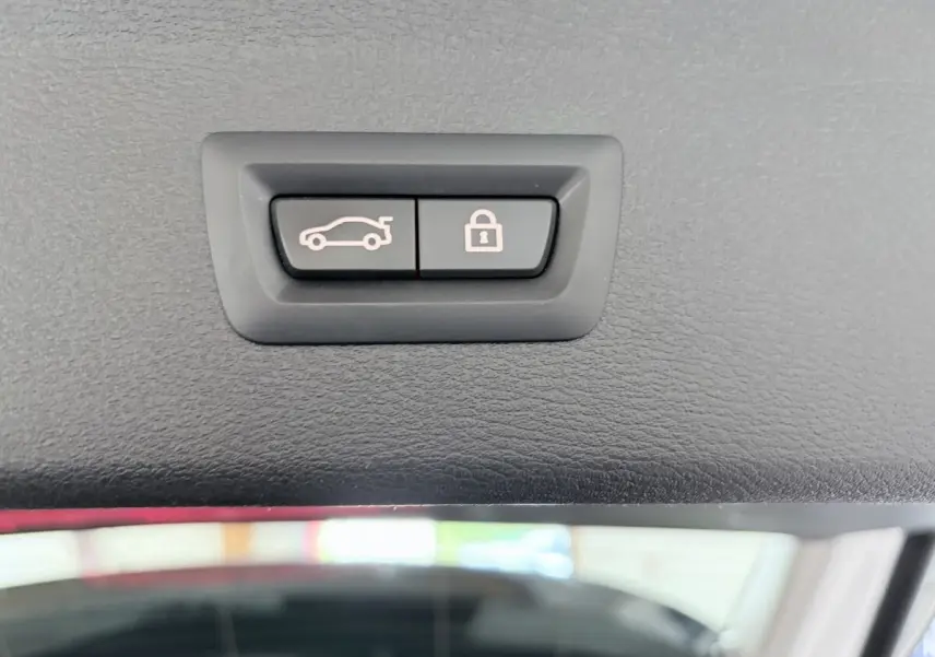 Gros plan sur les boutons d'ouverture et de verrouillage du coffre du BMW X1 blanc xDrive25eA xLine 2021.