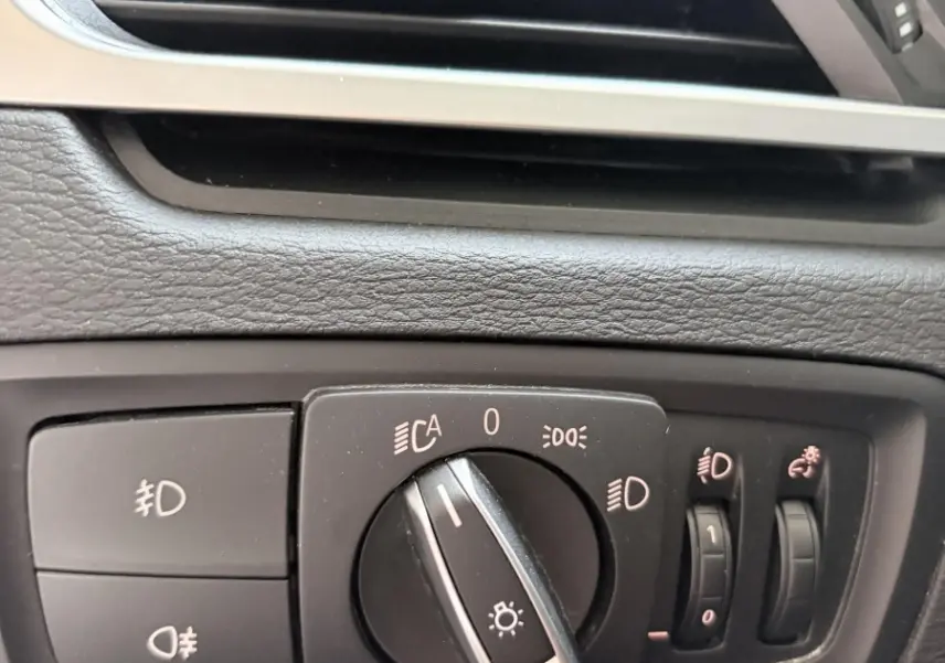 Gros plan sur les commandes d’éclairage et la sortie d’air du tableau de bord intérieur d’une BMW X1 blanche.