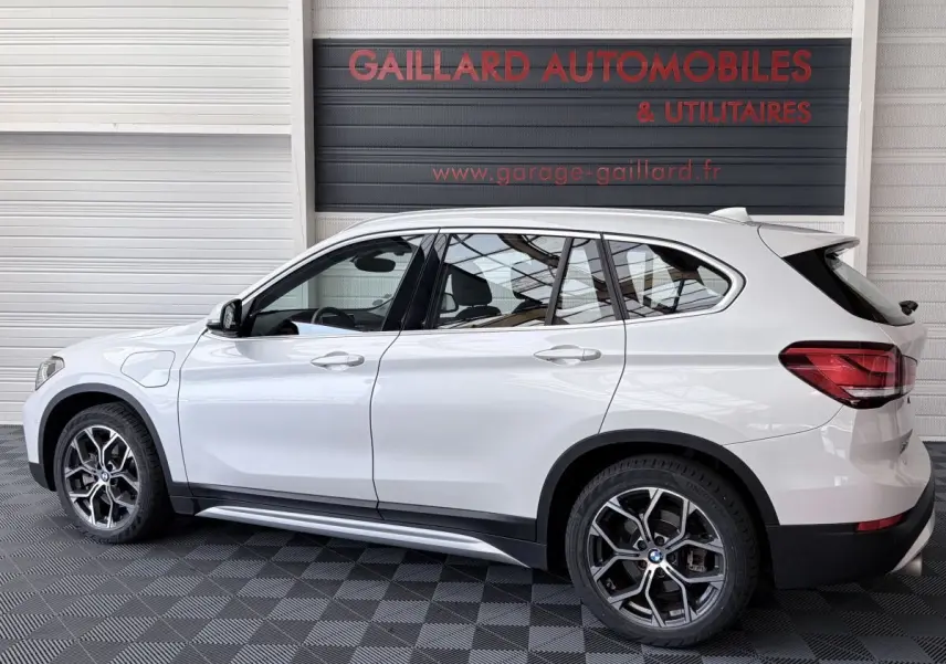 Vue latérale droite d’un BMW X1 blanc hybride rechargeable avec jantes alliage et rails de toit chromés.