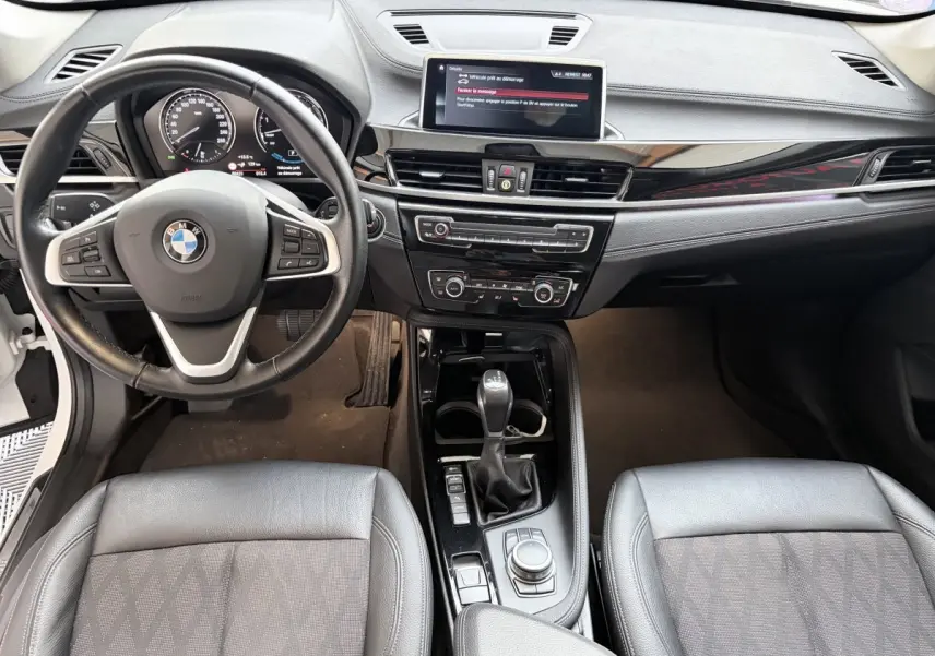 Vue intérieure avant de la BMW X1 xDrive25eA xLine 2021, volant cuir alu multifonctions et console centrale noire brillante.