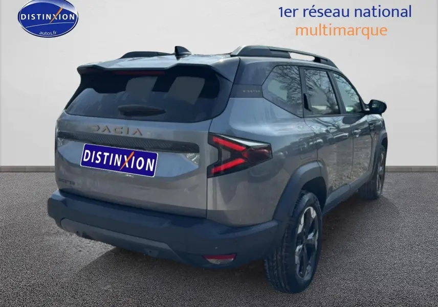 Vue 3/4 arrière droit du SUV Dacia Bigster gris schiste avec barres de toit et feux arrière LED en forme de flèche.