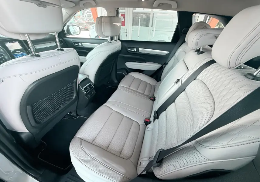 Vue intérieure arrière du Renault Koleos blanc 2021, sièges cuir beige clair avec surpiqûres et ceintures noires.