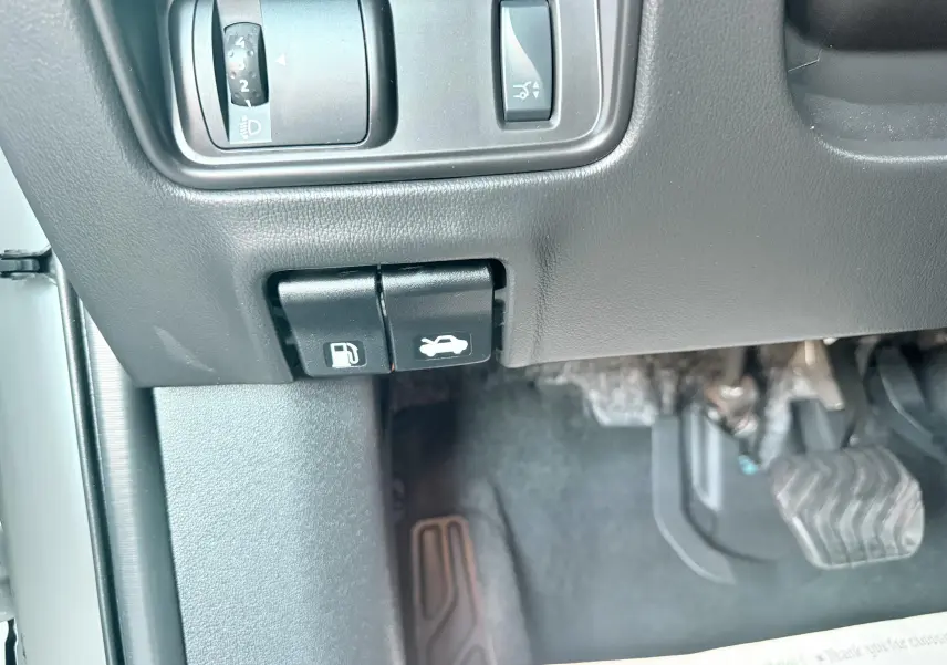 Gros plan sur les commandes d'ouverture du capot et de la trappe à carburant côté gauche d'un Renault Koleos blanc, 2021.