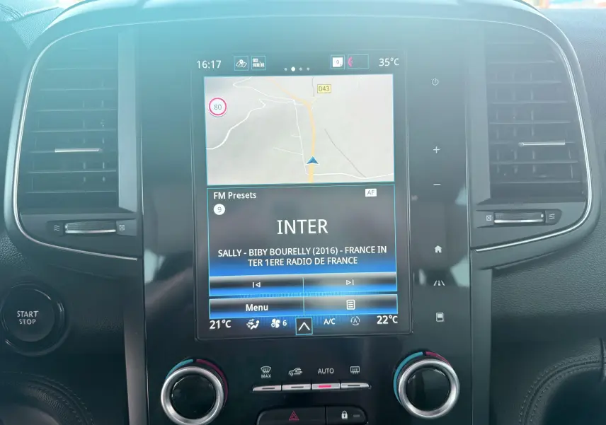 Vue rapprochée de l’écran tactile central du tableau de bord du Renault Koleos blanc, affichant la navigation et la radio.