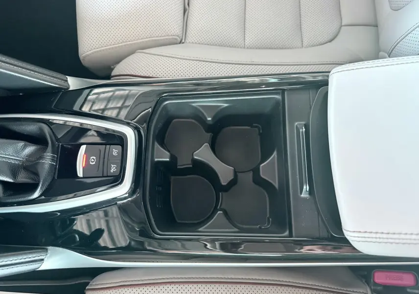 Vue plongeante sur la console centrale noire avec porte-gobelets et accoudoir beige perforé du Renault Koleos blanc.