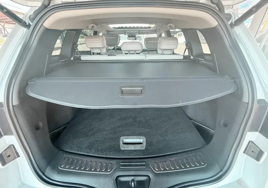 Coffre ouvert vu de l'arrière d'un Renault Koleos blanc, avec cache-bagages et sièges arrière beige visibles.