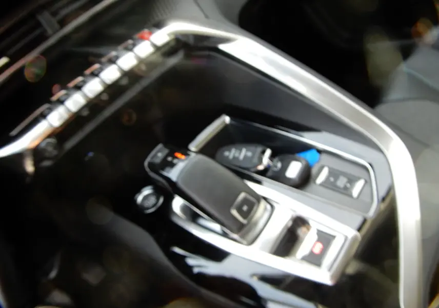 Gros plan sur la console centrale noire brillante du Peugeot 5008 blanc nacré, mettant en valeur le levier de vitesses automatique.