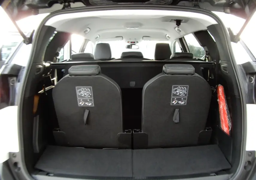 Vue arrière ouverte du coffre d'un Peugeot 5008 blanc nacré, montrant les dossiers des sièges rabattus et les appuie-têtes noirs.