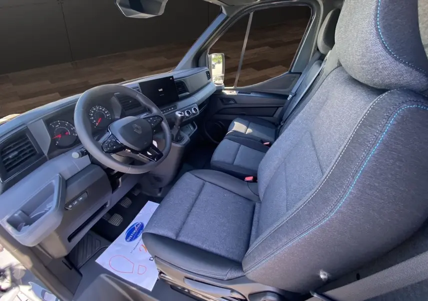 Intérieur du Renault Master 2025 vu côté conducteur, sièges gris chiné avec surpiqûres bleues et tableau de bord moderne.