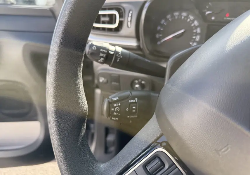 Gros plan sur le volant et le tableau de bord de la Citroën C3 gris acier, montrant les commandes au volant et les compteurs.