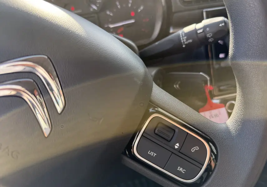 Gros plan sur le volant noir de la Citroën C3 gris acier 2023, avec commandes audio intégrées visibles.