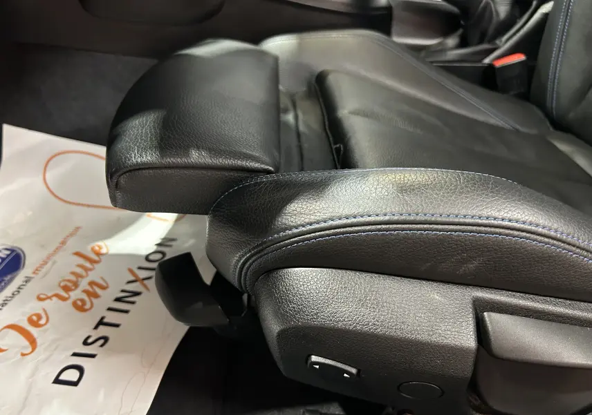 Gros plan sur le siège avant en cuir noir avec surpiqûres bleues de la BMW Série 1 120iA M Sport blanche.