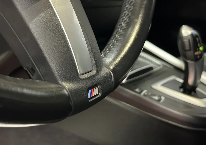 Gros plan sur le volant cuir noir avec logo M et levier de vitesse automatique de la BMW Série 1 120iA M Sport blanche.
