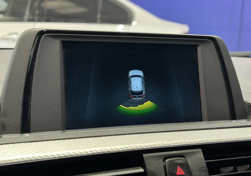 Écran intérieur montrant l'alerte radar de recul d'une BMW Série 1 blanche, version 120iA M Sport de 2019.