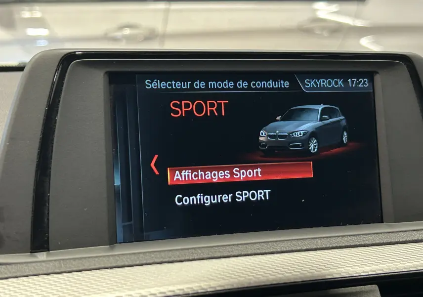 Écran intérieur BMW Série 1 affichant le mode de conduite Sport avec une voiture grise en vue 3/4 avant.