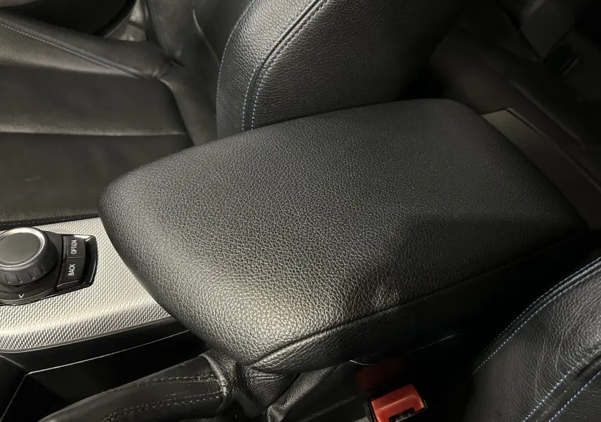 Gros plan sur l'accoudoir central en cuir noir avec surpiqûres bleues dans l'habitacle d'une BMW Série 1 blanche.