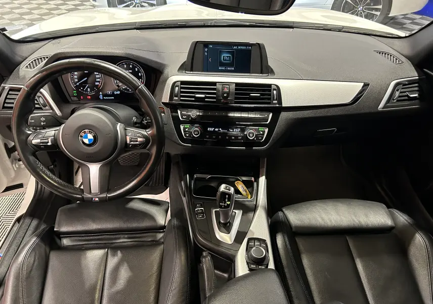 Vue intérieure avant de la BMW Série 1 120iA M Sport 2019, volant cuir multifonction et console centrale avec écran multimédia.