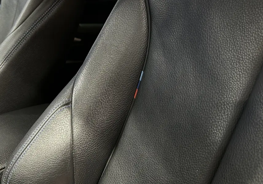 Gros plan sur le siège avant en cuir noir de la BMW Série 1 120iA M Sport avec surpiqûres bleues et détail tricolore.