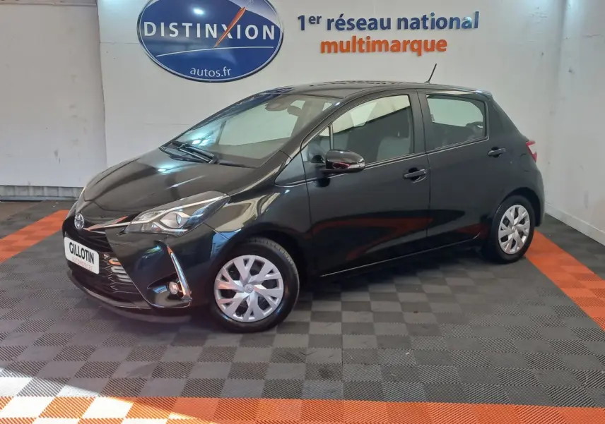 Toyota Yaris 1.5 VVT-I Hybrid noire vue de profil avant droit en intérieur sur sol damier gris et orange.