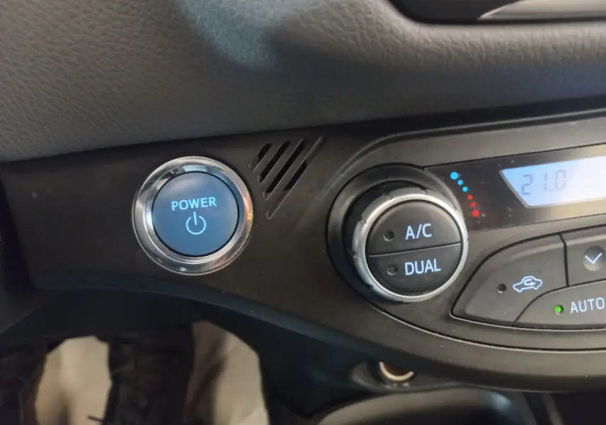 Détail du tableau de bord noir de la Toyota Yaris hybride 2018 avec bouton démarrage bleu et commandes climatisation digitale.