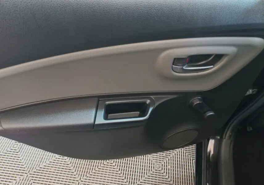 Intérieur côté gauche de la porte d'une Toyota Yaris noire, avec poignée argentée et commande manuelle de vitre.