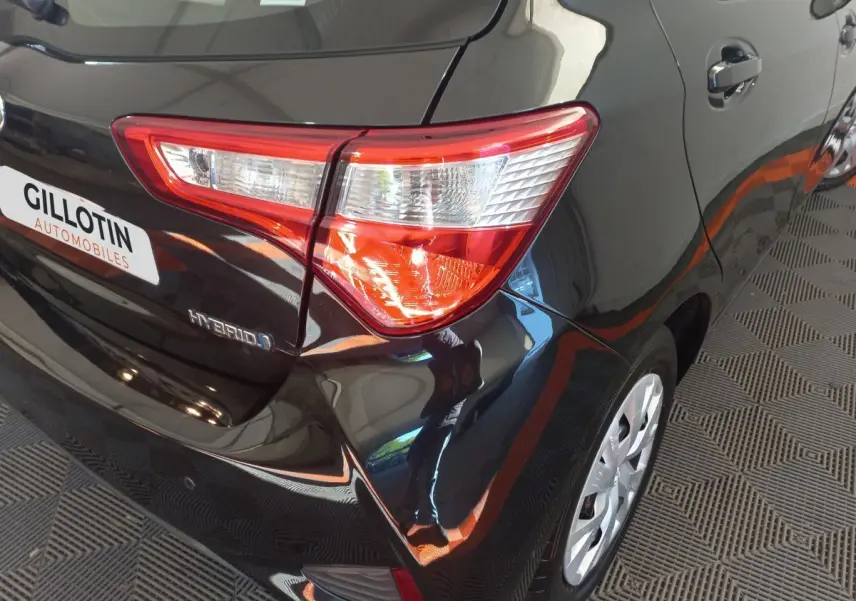 Vue 3/4 arrière droite d'une Toyota Yaris noire hybride, avec feu arrière distinctif et jante visible.