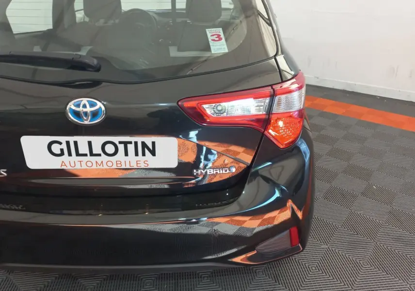 Vue arrière droite d'une Toyota Yaris hybride noire avec feux arrière distinctifs et logo Hybrid visible.