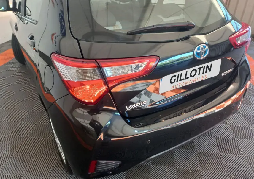 Vue 3/4 arrière gauche d'une Toyota Yaris noire hybride avec feux arrière distinctifs et logo visible sur hayon.