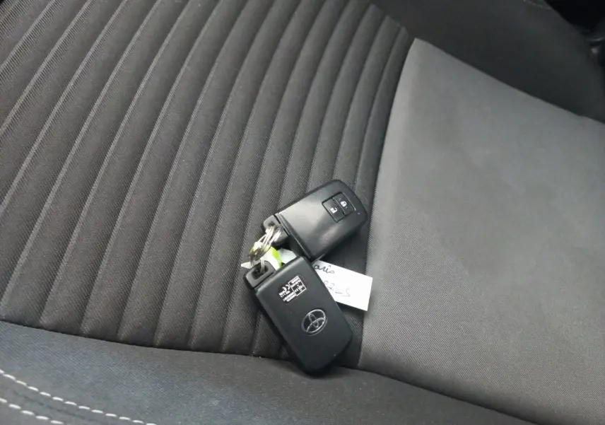 Clé de voiture Toyota posée sur un siège avant en tissu noir à motifs rayés, intérieur sobre et moderne.