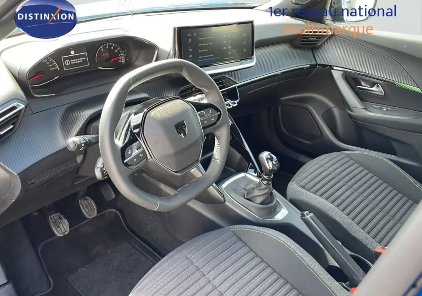 Vue intérieure côté conducteur du Peugeot 2008 2024, montrant le volant, la boîte manuelle et les sièges tissu noir avec surpiqûres vertes.