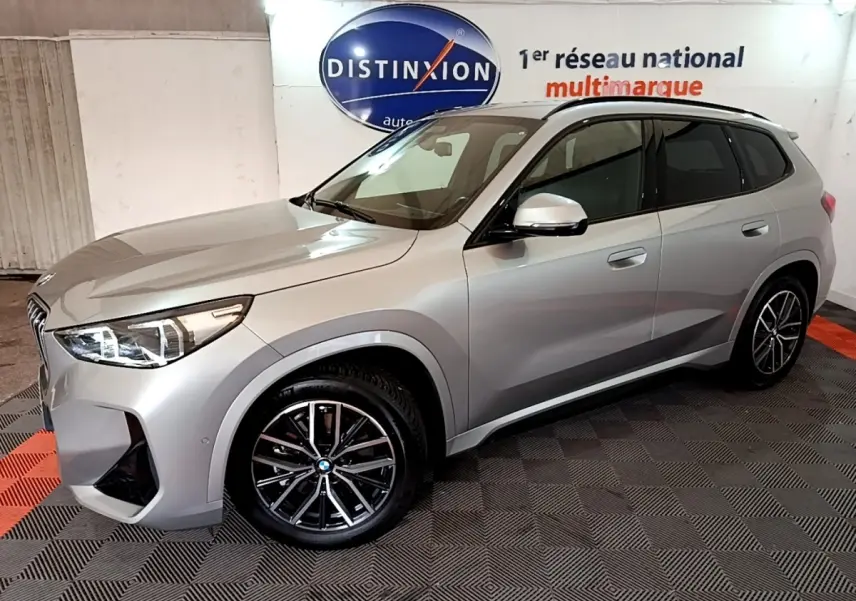 BMW X1 xDrive23i M Sport gris clair vue de profil droit en intérieur avec jantes noires et toit noir.