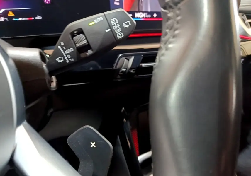 Gros plan sur la commande d'essuie-glace et palette de changement de vitesse derrière le volant cuir d’un BMW X1 gris clair.