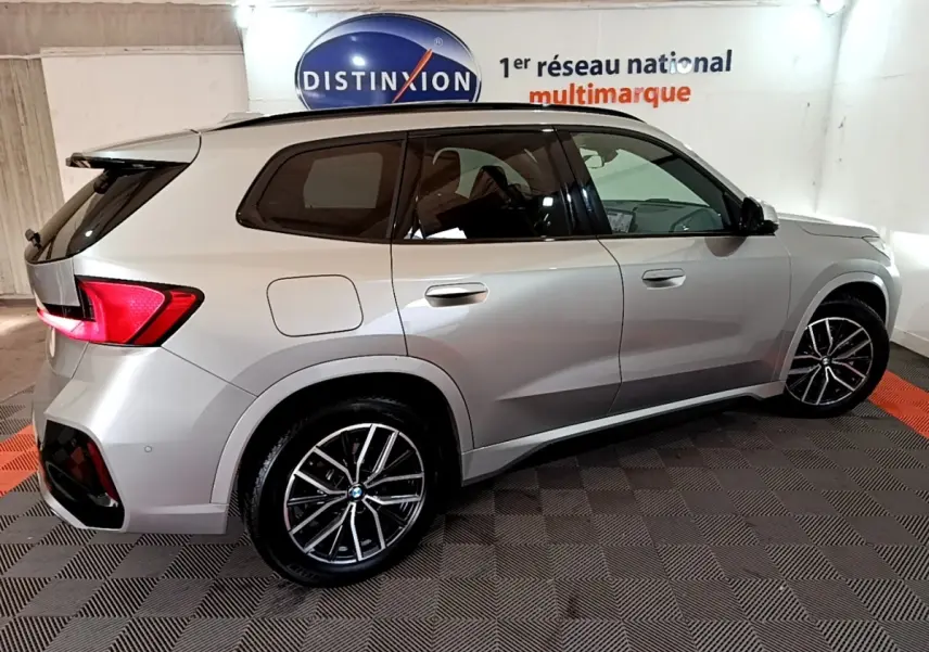 BMW X1 xDrive23i M Sport gris clair vue de profil côté droit dans un showroom avec jantes alliage noires.