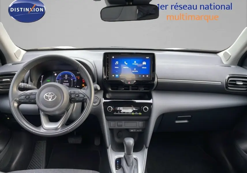 Vue frontale de l'intérieur de la Toyota Yaris Cross 2024, tableau de bord noir avec écran tactile central et volant multifonction.