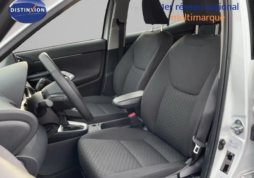 Vue intérieure côté conducteur de la Toyota Yaris Cross 2024 blanche, sièges tissu gris et volant cuir multifonction.