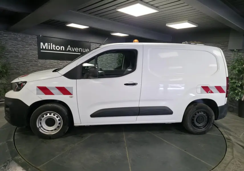 Vue de profil côté gauche d’un Peugeot Partner blanc avec bandes réfléchissantes rouges et blanches sur ailes avant et arrière.