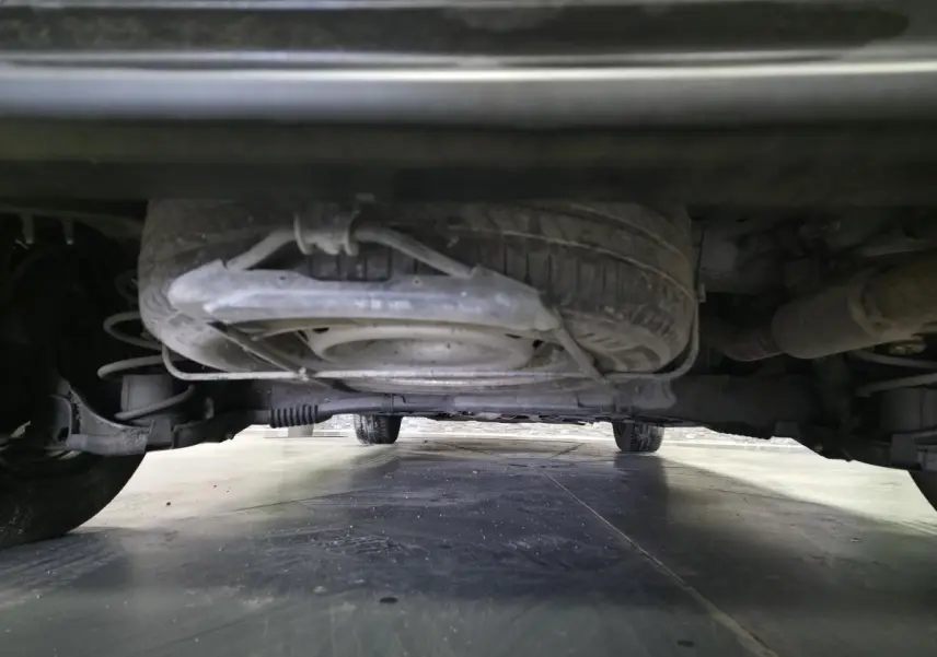 Vue en contre-plongée sous le Peugeot Partner blanc, montrant la roue de secours et le châssis arrière.