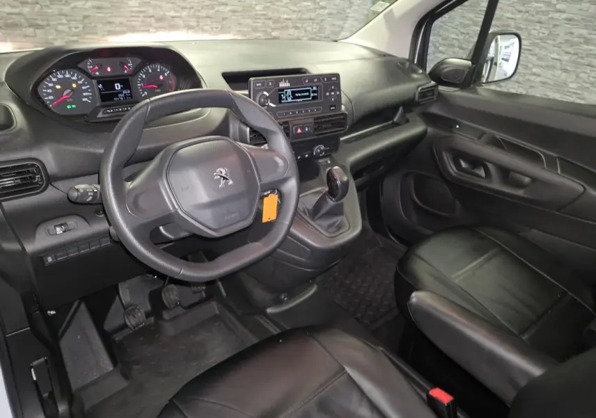 Intérieur du Peugeot Partner 2021 vu côté conducteur, tableau de bord noir avec volant et sièges en cuir noir.