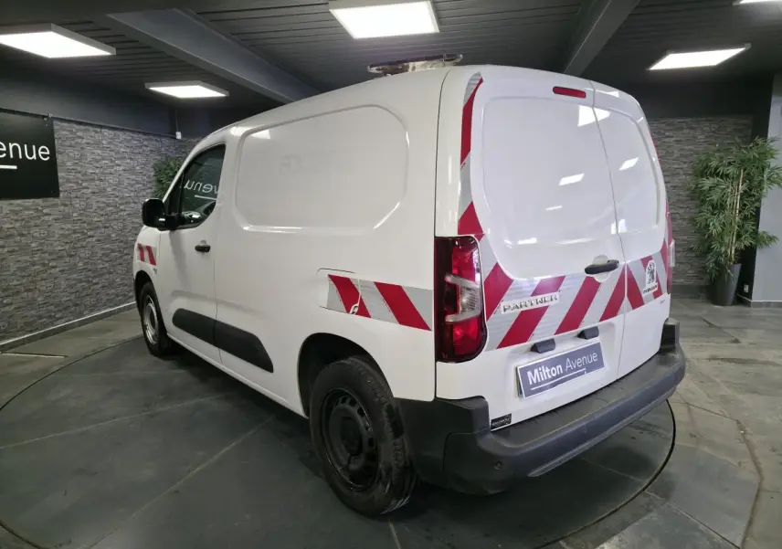 Vue 3/4 arrière droite d’un Peugeot Partner blanc avec bandes réfléchissantes rouges et blanches sur les portes arrière et latérales.