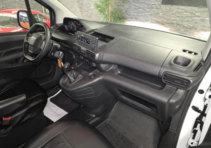 Intérieur avant droit du Peugeot Partner 2021, tableau de bord noir avec volant, levier de vitesse manuel et sièges en cuir noir.