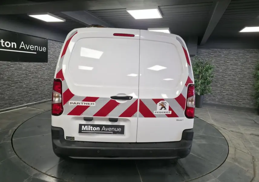 Vue arrière d'un Peugeot Partner blanc avec bandes réfléchissantes rouges et blanches et portes battantes tôlées.